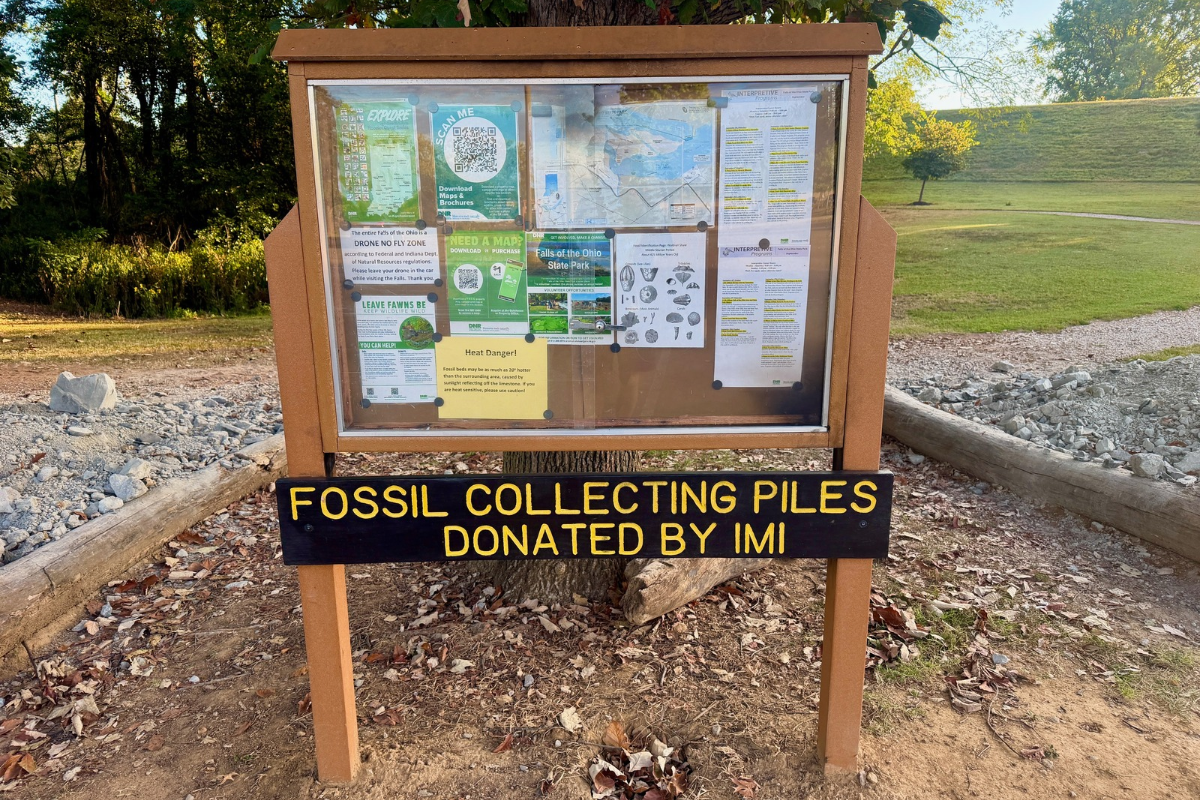 Two rock collecting piles beside an information board and a sign reading “Fossil Collecting Piles Donated by IMI”