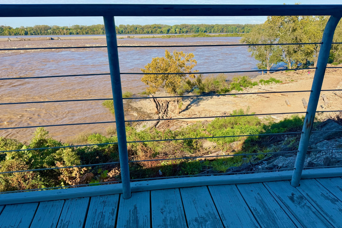 View through an observation deck railing toward exposed rock slabs, riverside trees, and the Ohio River